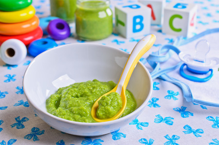 Puree of green in the small bowl is on the background of childrens toysの写真素材