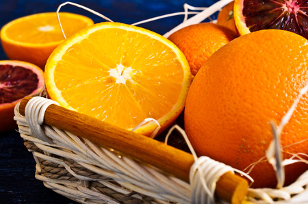 Whole and sliced fruit in a wicker basket with straw on painted wood surfacesの写真素材
