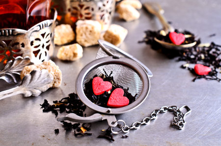 Tea with sweets in the shape of a heart against a metal strainer