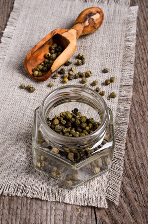 Green peppercorns in a glass jar on burlapの写真素材