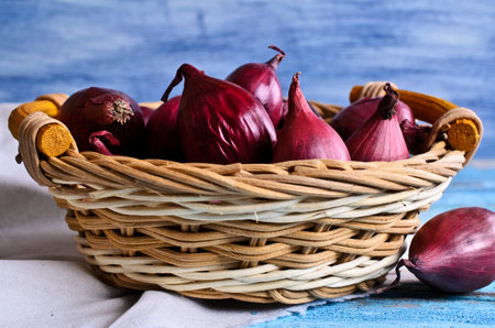 Red onion in a wicker basket on a wooden surfaceの写真素材