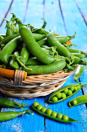 Fresh green peas in a wicker basket on a wooden surfaceの写真素材
