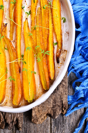 Baked carrots in a baking dish with vegetable oil on a wooden surfaceの写真素材