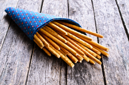 Bread sticks, long and thin, in a paper envelope lying on a wooden surface.の写真素材