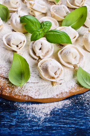 Tortelli raw, sprinkled with flour, Basil leaves on a wooden surfaceの写真素材