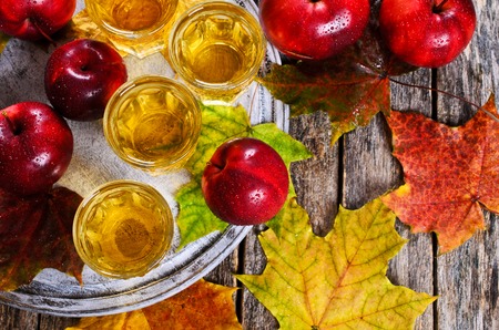 Apple drink in a transparent glass on a wooden surface on a background of red apples and maple leavesの写真素材