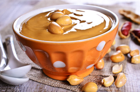 Peanut butter in a ceramic dish on the background of whole nuts. Selective focus.