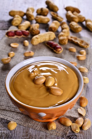 Peanut butter in a ceramic dish on the background of whole nuts. Selective focus.の写真素材