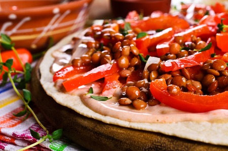 Thin flat bread with sauce, lentils and vegetables on a wooden surfaceの写真素材