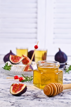 Liquid golden honey in jar on background camembert, fig and rosemary. Selective focus.の写真素材