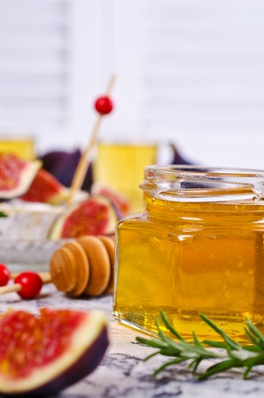 Liquid golden honey in jar on background camembert, fig and rosemary. Selective focus.の写真素材
