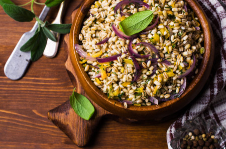 Boiled pearl barley with vegetables and herbs on a wooden background. Selective focus.の写真素材