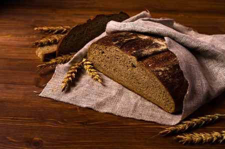 Cut dark bread on a wooden background with rye ears. Selective focus.の写真素材