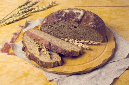 Cut dark bread on a wooden background with rye ears. Selective focus.