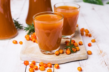 Thick orange drink in the glass on a wooden background with sea buckthorn berries. Selective focus.の写真素材