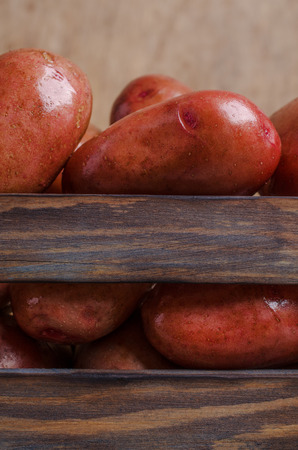 Large washed potatoes in a box on wooden background. Selective focus.の写真素材