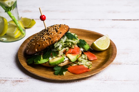 Burger with salted salmon and vegetables on wooden background. Selective focus.の写真素材