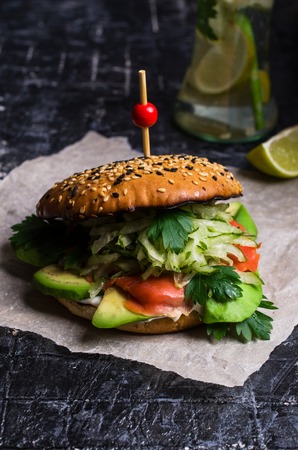 Burger with salted salmon and vegetables on wooden background. Selective focus.の写真素材