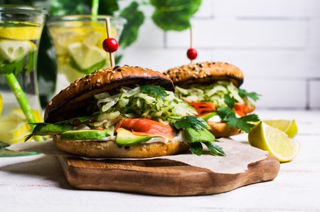 Burger with salted salmon and vegetables on wooden background. Selective focus.の写真素材