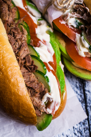 Sandwich with meat, vegetables and white sauce on wooden background. Selective focus.の写真素材