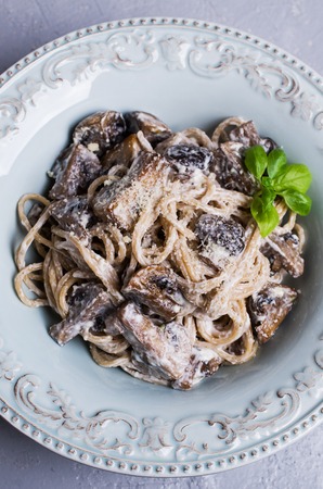 Dark spaghetti with mushrooms and white sauce in a plate on the table. Selective focus.の写真素材