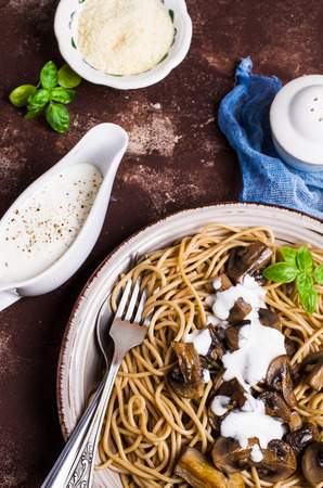 Dark spaghetti with mushrooms and white sauce in a plate on the table. Selective focus.の写真素材