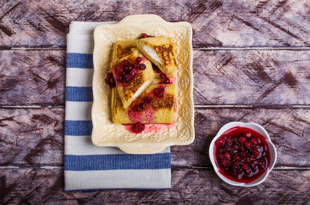 Pancakes with white filling and berry confiture in plate on wooden background. Selective focus.の写真素材