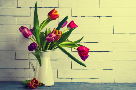 Bouquet of multicolored tulips in a vase on the table by the wall. Selective focus.の写真素材
