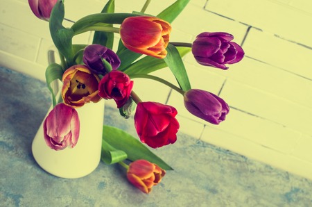 Bouquet of multicolored tulips in a vase on the table by the wall. Selective focus.の写真素材