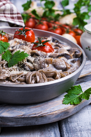Dark pasta with vegetables in white sauce on wooden background. Selective focus.の写真素材
