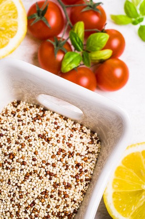Dry mixture of quinoa grains on wooden background with tomatoes and lemon. Selective focus.の写真素材