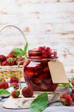 Slices of red strawberries with syrup in a glass jar on a wooden table. Selective focus.の写真素材