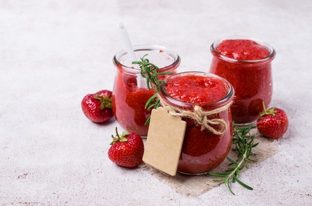 Red strawberry jam in a glass jar on the table. Selective focus.の写真素材