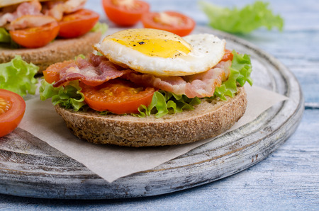 Traditional sandwich with fried bacon, tomatoes and egg on wooden background. Selective focus.の写真素材