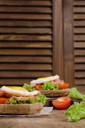 Traditional sandwich with fried bacon, tomatoes and egg on wooden background. Selective focus.の写真素材