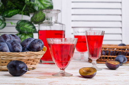 Transparent red drink in glass with fresh plums on wooden background. Selective focus.の写真素材