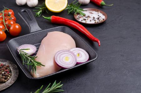 Raw chicken breast with vegetables and spices on dark background. Selective focus.の写真素材