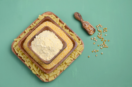 Dry corn products. Grains, polenta, flour, pasta. Green wooden background. Selective focus.の写真素材