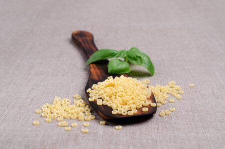 Dry small pasta with basil leaves on textile background. Selective focus.の写真素材