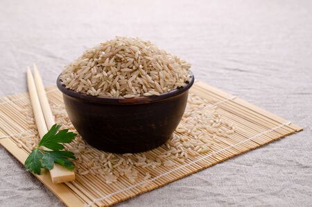 Brown unpolished rice in ceramic bowl on textile background. Selective focus.の写真素材
