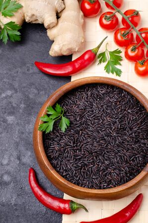 Black unpolished rice in a wooden bowl on a slate background. Selective focus.の写真素材