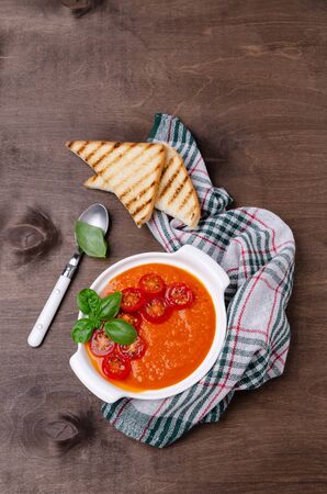 Homemade vegetable red cream soup with slices of fried tomatoes and Basil on a wooden background. Selective focus.の写真素材