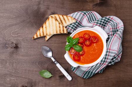 Homemade vegetable red cream soup with slices of fried tomatoes and Basil on a wooden background. Selective focus.の写真素材