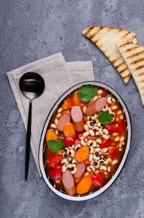 Stewed beans with sausages and vegetables in a ceramic dish. Selective focus.の写真素材