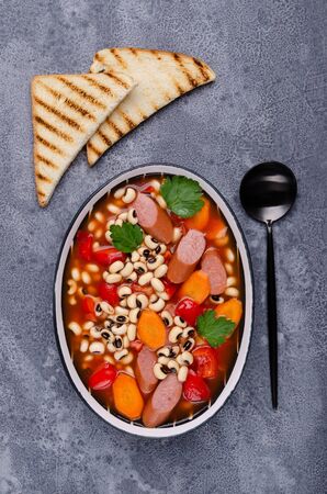 Stewed beans with sausages and vegetables in a ceramic dish. Selective focus.の写真素材