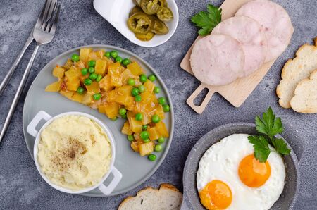 Breakfast serving concept. Stewed zucchini, fried eggs, mashed potatoes, slices of meat. Grey slate background. Selective focus.の写真素材