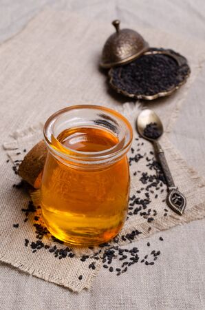 Glass jar with oil. Black sesame seeds. Textile background. Selective focus.の写真素材