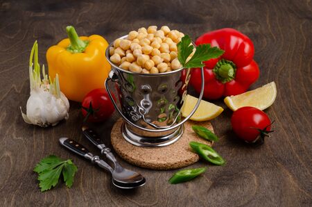 Canned chickpeas in a tin a tin on a dark wooden background with raw vegetables. Selective focus.の写真素材