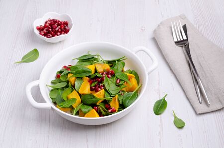 Spinach salad and baked pumpkin with pomegranate seeds in a dish on a wooden background. Selective focus.の写真素材