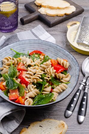 Brown pasta with vegetables, nuts and cheese in a dish on a wooden background. Selective focus.の写真素材